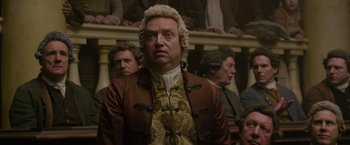 Movie still from “Pirates of the Caribbean: On Stranger Tides” (2011), directed by Rob Marshall – A man in a wig and wig stands in front of a group of people; Medium shot, Over the shoulder angle