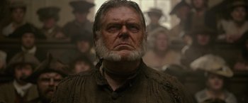 An old man with a beard is looking at the camera