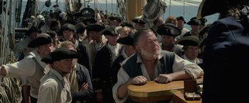 Movie still from “Pirates of the Caribbean: On Stranger Tides” (2011), directed by Rob Marshall – A group of people in hats and vests standing around a table; Medium shot, Over the shoulder angle