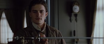 Movie still from “Pirates of the Caribbean: The Curse of the Black Pearl” (2003), directed by Gore Verbinski – A young man holding a sword in a room; Close Up shot, Low angle