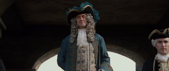 Movie still from “Pirates of the Caribbean: The Curse of the Black Pearl” (2003), directed by Gore Verbinski – A man in a wig and wig stands in front of an archway; Medium shot, Low angle