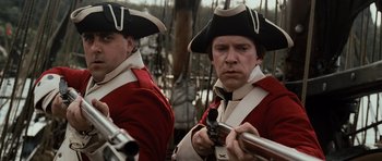 Movie still from “Pirates of the Caribbean: The Curse of the Black Pearl” (2003), directed by Gore Verbinski – Two men in red and white uniforms holding guns; Close Up shot, Low angle