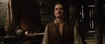 Movie still from “Pirates of the Caribbean: The Curse of the Black Pearl” (2003), directed by Gore Verbinski – A man wearing a brown vest standing next to a fire pit; Medium shot, Low angle