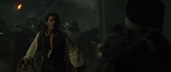 Movie still from “Pirates of the Caribbean: The Curse of the Black Pearl” (2003), directed by Gore Verbinski – A man standing next to a group of people in a dark room; Medium shot, Over the shoulder angle