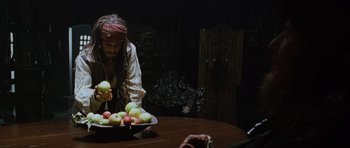 Movie still from “Pirates of the Caribbean: The Curse of the Black Pearl” (2003), directed by Gore Verbinski – A man in a pirate's outfit is looking at apples in a bowl on a table; Medium shot, High angle