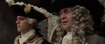 Movie still from “Pirates of the Caribbean: The Curse of the Black Pearl” (2003), directed by Gore Verbinski – A man in a wig and a man in a suit and a hat; Close Up shot, Over the shoulder angle