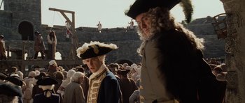 Movie still from “Pirates of the Caribbean: The Curse of the Black Pearl” (2003), directed by Gore Verbinski – Two men in period dress standing next to each other in front of a crowd of onlookers; Medium shot, Low angle