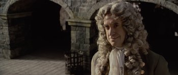 Movie still from “Pirates of the Caribbean: The Curse of the Black Pearl” (2003), directed by Gore Verbinski – A man in a wig and wig stands in front of a stone wall; Close Up shot, Over the shoulder angle