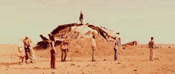 Movie still from “Pitch Black” (2000), directed by David Twohy – A group of people standing on top of a pile of rubble; Wide shot, Low angle