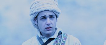 Movie still from “Pitch Black” (2000), directed by David Twohy – A young man wearing a white turban and a striped shirt; Close Up shot, Over the shoulder angle