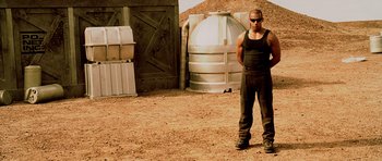 Movie still from “Pitch Black” (2000), directed by David Twohy – A man standing in front of a metal tank; Medium shot, Low angle