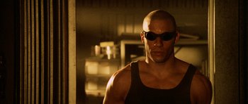 Movie still from “Pitch Black” (2000), directed by David Twohy – A bald man wearing sunglasses and a black tank top; Close Up shot, Low angle