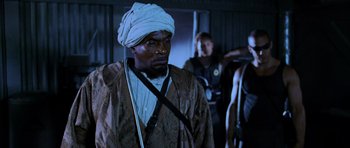 Movie still from “Pitch Black” (2000), directed by David Twohy – A man with a white turban and a brown jacket; Medium shot, Low angle