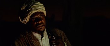 Movie still from “Pitch Black” (2000), directed by David Twohy – A man with a white turban holding a cell phone in a dark room; Close Up shot, Low angle