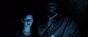 Movie still from “Pitch Black” (2000), directed by David Twohy – A man standing next to a young boy in a dark room; Medium shot, Low angle