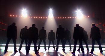 Movie still from “Pitch Perfect” (2012), directed by Jason Moore – A group of men standing in front of a stage; Wide shot, Low angle