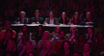 Movie still from “Pitch Perfect” (2012), directed by Jason Moore – A group of people sitting at a table in front of a crowd; Wide shot, High angle