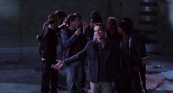 Movie still from “Pitch Perfect” (2012), directed by Jason Moore – A group of people standing around a man in the dark; Medium shot, High angle