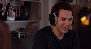 Movie still from “Pitch Perfect” (2012), directed by Jason Moore – A young man wearing headphones while sitting on a couch; Close Up shot, Over the shoulder angle