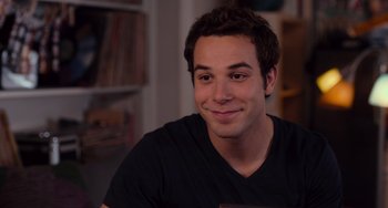 Movie still from “Pitch Perfect” (2012), directed by Jason Moore – A young man smiling for the camera in a living room; Close Up shot, Over the shoulder angle