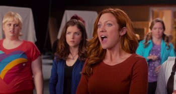 Movie still from “Pitch Perfect” (2012), directed by Jason Moore – Two women standing next to each other and one of them has a surprised look on her face; Medium shot, Over the shoulder angle