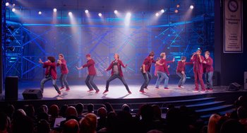 Movie still from “Pitch Perfect” (2012), directed by Jason Moore – A group of young men on a stage performing a dance move; Wide shot, High angle