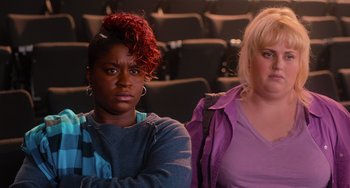 Movie still from “Pitch Perfect” (2012), directed by Jason Moore – Two women sitting in front of each other in front of a movie screen; Close Up shot, High angle
