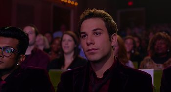 Movie still from “Pitch Perfect” (2012), directed by Jason Moore – A young man sitting in front of an audience in front of a crowd; Close Up shot, Over the shoulder angle