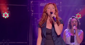 Movie still from “Pitch Perfect” (2012), directed by Jason Moore – A woman with long red hair singing into a microphone; Medium shot, Over the shoulder angle
