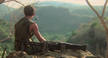 Movie still from “Platoon” (1986), directed by Oliver Stone – A man sitting on top of a mountain holding a gun; Wide shot, High angle