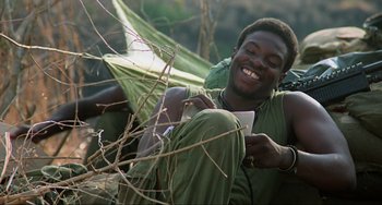 Movie still from “Platoon” (1986), directed by Oliver Stone – A man sitting on the ground while holding a paper in his hand; Close Up shot, High angle