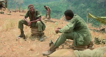 Movie still from “Platoon” (1986), directed by Oliver Stone – A group of men sitting on top of a tree stump; Medium shot, High angle