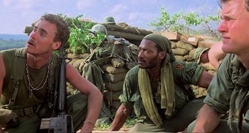 Movie still from “Platoon” (1986), directed by Oliver Stone – A man sitting on the ground in front of a pile of dirt; Medium shot, Low angle