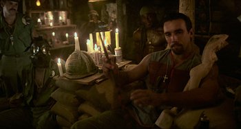 Movie still from “Platoon” (1986), directed by Oliver Stone – A man sitting in front of a group of lit candles; Medium shot, High angle