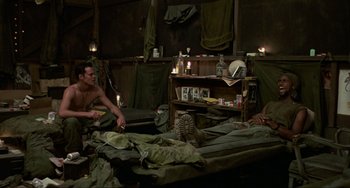 Movie still from “Platoon” (1986), directed by Oliver Stone – A man and a woman sitting on a bed in a tent; Wide shot, High angle