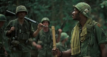 Movie still from “Platoon” (1986), directed by Oliver Stone – A group of men in fatigues and hats are standing in the woods; Medium shot, Low angle