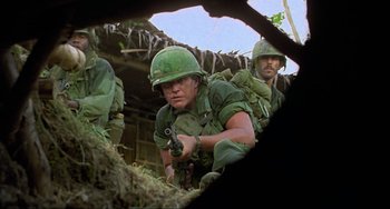 Movie still from “Platoon” (1986), directed by Oliver Stone – A group of men in green uniforms are standing in the dirt; Medium shot, Low angle