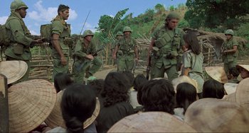 Movie still from “Platoon” (1986), directed by Oliver Stone – A group of men standing next to each other in front of a crowd of onlookers; Wide shot, High angle