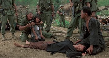 Movie still from “Platoon” (1986), directed by Oliver Stone – A group of people standing next to a person laying on the ground; Medium shot, High angle
