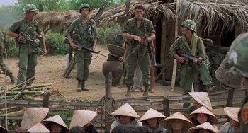 Movie still from “Platoon” (1986), directed by Oliver Stone – A group of men standing next to each other in a field; Wide shot, Over the shoulder angle