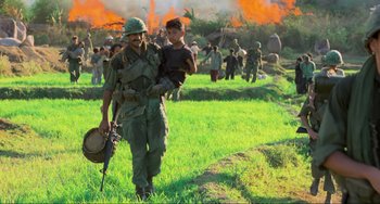 Movie still from “Platoon” (1986), directed by Oliver Stone – A man carrying a child walking through a field; Wide shot, Low angle
