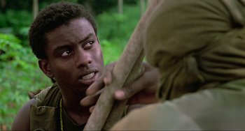 Movie still from “Platoon” (1986), directed by Oliver Stone – A young man holding a tree branch while another man looks on; Close Up shot, Over the shoulder angle