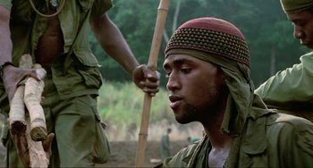 Movie still from “Platoon” (1986), directed by Oliver Stone – A man with a hat on and a stick in his hand; Close Up shot, Over the shoulder angle