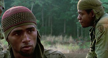 Movie still from “Platoon” (1986), directed by Oliver Stone – Two men are standing in the woods looking at the camera; Close Up shot, Over the shoulder angle