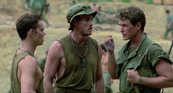 Movie still from “Platoon” (1986), directed by Oliver Stone – A group of men standing next to each other on top of a field; Medium shot, Over the shoulder angle