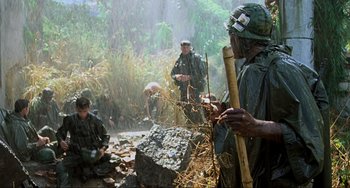 Movie still from “Platoon” (1986), directed by Oliver Stone – A group of men in rain gear are sitting in the woods; Wide shot, High angle