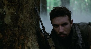 Movie still from “Platoon” (1986), directed by Oliver Stone – A man holding a rifle leaning up against a tree; Close Up shot, Low angle