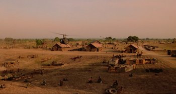 Movie still from “Platoon” (1986), directed by Oliver Stone – A helicopter is flying over a dirt field with people sitting in it; Extreme Wide shot, High angle
