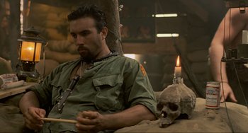 Movie still from “Platoon” (1986), directed by Oliver Stone – A man sitting next to a skull with a lit candle; Close Up shot, High angle