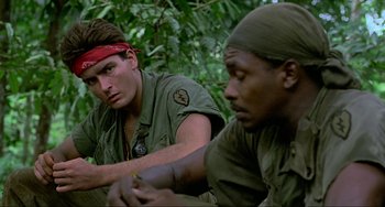 Movie still from “Platoon” (1986), directed by Oliver Stone – Two men sitting in the woods looking at each other; Close Up shot, Low angle